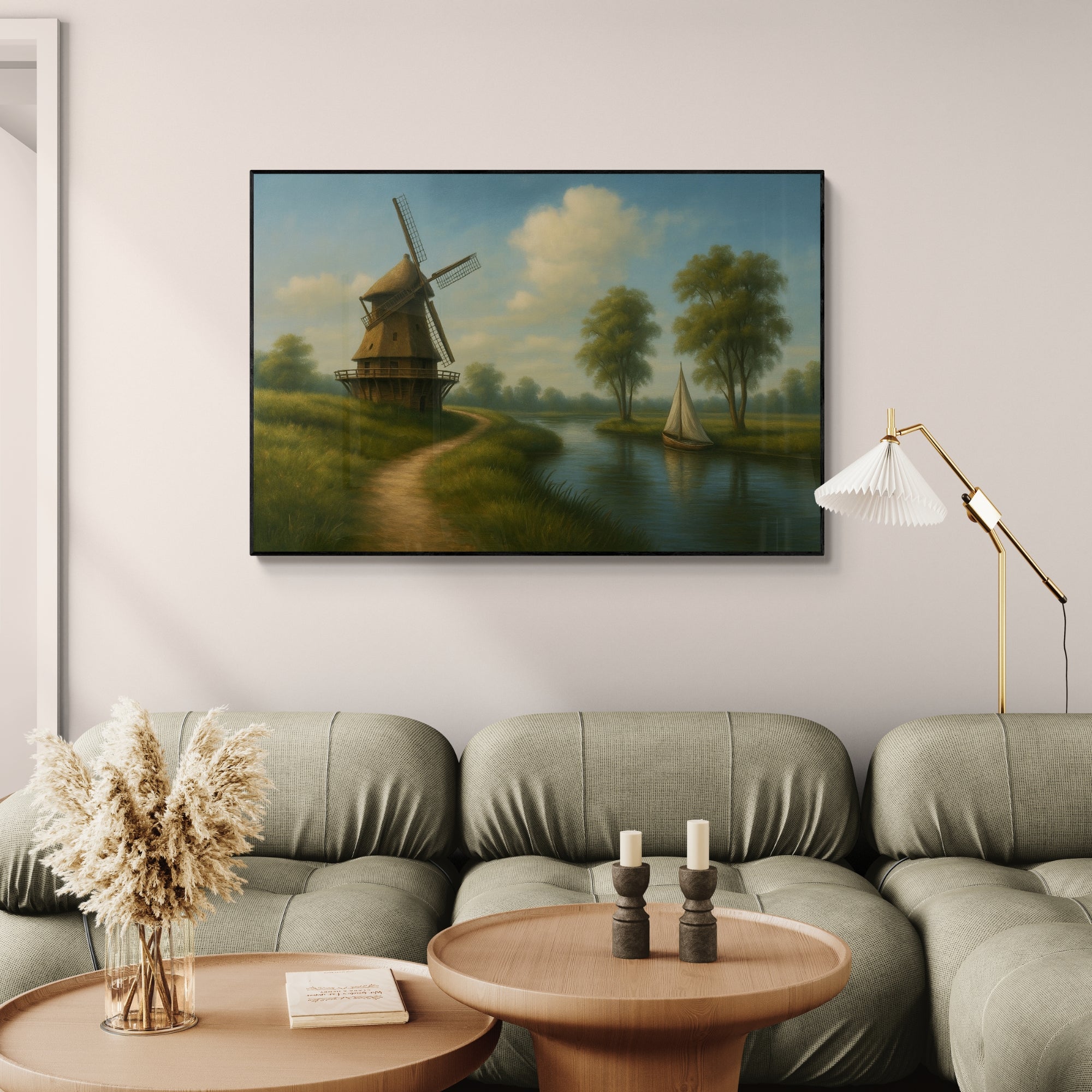 A framed oil painting depicting a Dutch countryside scene with a windmill, path, and sailboat on a river, displayed above a sofa in a cozy interior setting.