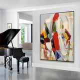 Bold abstract painting with sweeping brushstrokes in red, black, green, and yellow on a soft neutral background, displayed in a modern beige-toned living room.
