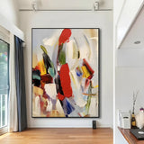 Colorful abstract artwork featuring vivid splashes of red, yellow, blue, and green, mounted on a clean white wall in a contemporary art gallery.